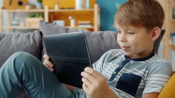Slow Motion of Smiling Child Holding Tablet Watching Video Indoors in Apartment alt