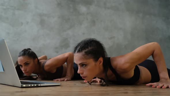 Young Sports Girls Twins Are Doing Sports Exercises Indoors at Home Using a Laptop Computer. The