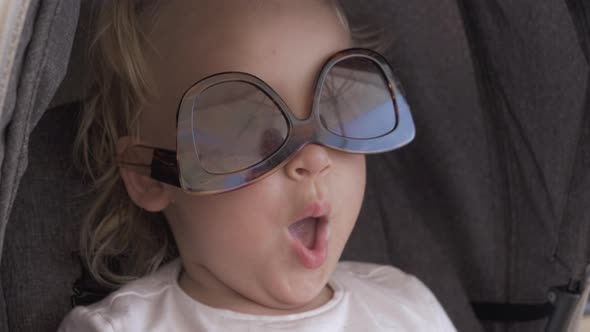 A closeup of a baby girls face who is wearing female sunglasses upside down