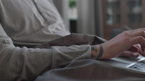 Man Typing On Laptop While Sitting In Bed