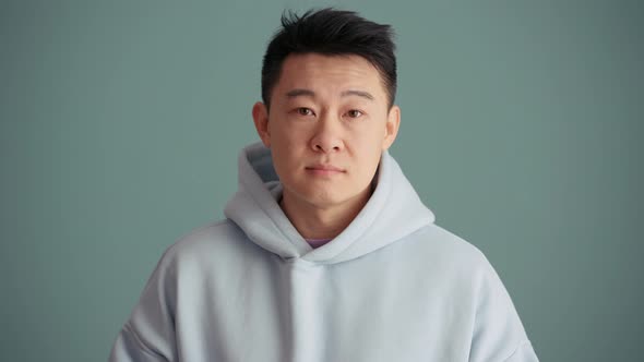 Cheerful Asian man wearing hoodie positively shaking his head