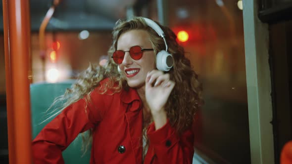 A Smiling Curly Woman in Headphones is Listening Music and Funny Dancing in Bus