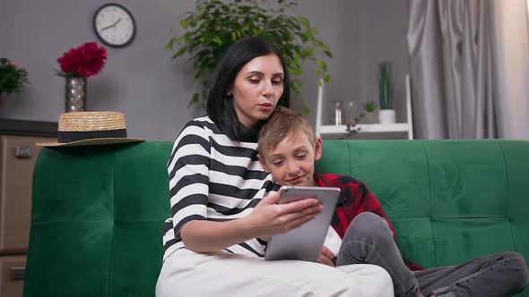 Modern Mother and Son Resting Together on Soft Couch at Home and Watching Intersting Apps