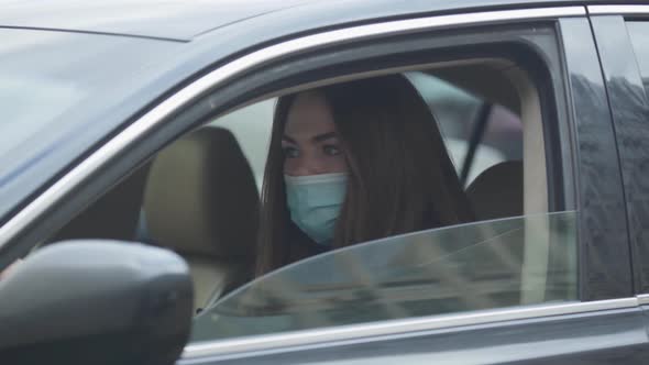 Side View Portrait of Young Woman in Protective Mask Sitting in Car and Coughing