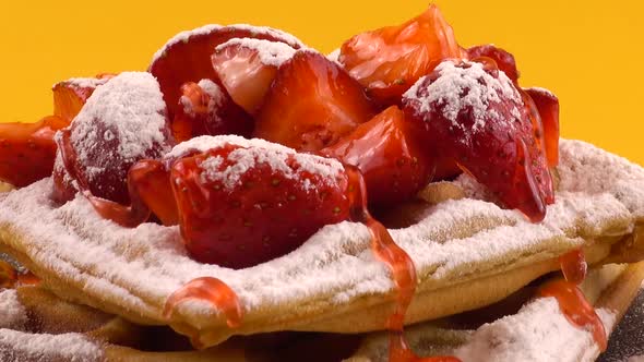 Belgian waffles with strawberry, sweet strawberry topping and powdered sugar on a stone board