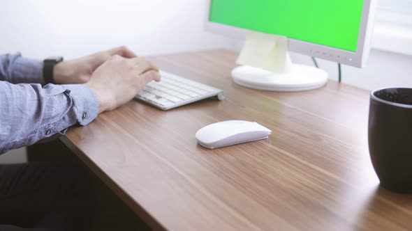 Young Worker Sitting By the Green Monitor and Typing Then Using His Smartwatch at His Desk to