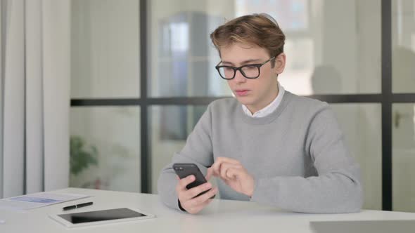 Attractive Young Man Using Smartphone in Modern Office