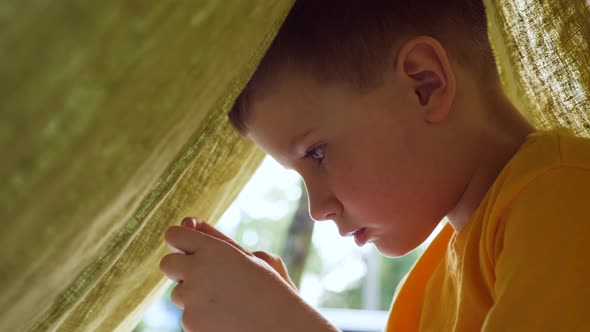 Boy Alone in the House with a Blanket Playing a Computer Game on a Smartphone. Technology Generation