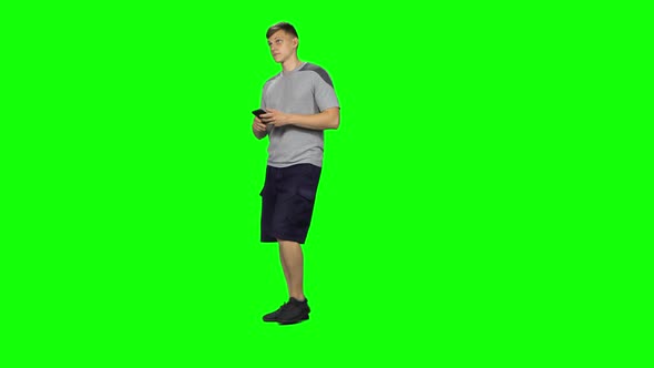 Smiling Man Goes and Texting with Smartphone on Green Screen at Studio.