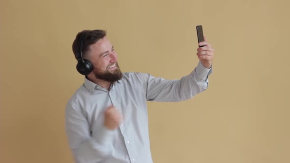 Man Stands on a Pastel Beige Background with Headphones on His Head and Talks