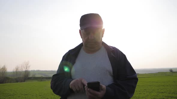 Mature Farmer Examining Soil and Using Smartphone Checking Report of Agriculture in a Field.