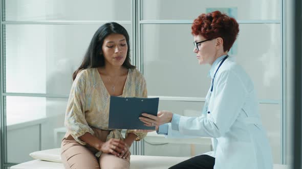 Hispanic Woman Signing Consent Form with Female Doctor in Clinic