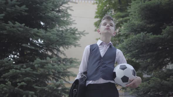 Handsome Well-dressed Boy Standing on the Street Holding the Soccer Ball and Purse