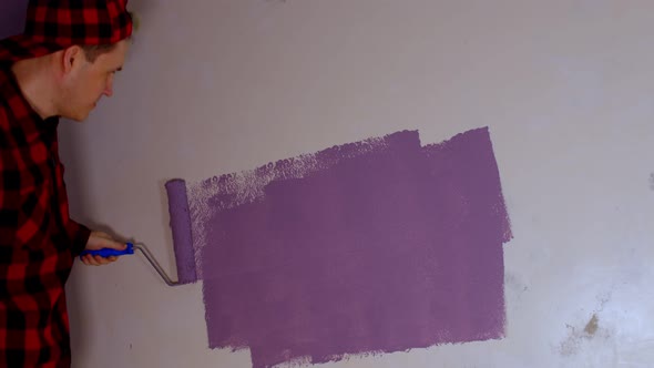 Close Up of Young Man Dancing and Painting Wall in Purple Colour with Roller