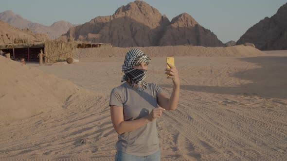 Woman in Checkered Keffiyeh Trying to Find Mobile Network Using Cell Phone Standing in Desert