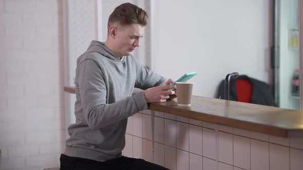 Absorbed Millennial Caucasian Young Man Sitting at Counter in Cafe Messaging Online in Tablet App