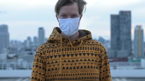 Face of Young Man with Mask Showing Stop Gesture Against View of the City