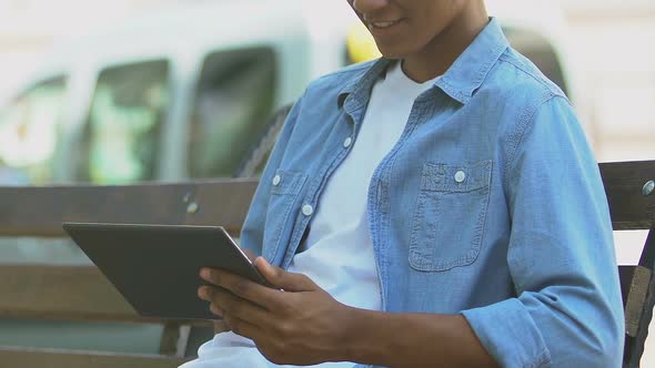 African-American teen boy scrolling tab on bench outdoors