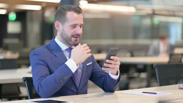 Middle Aged Businessman Celebrating Success on Smartphone at Work