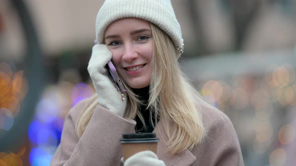 Young Lady with a cup of hot coffee is talking on her Mobile Phon