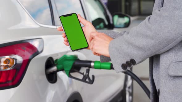 Woman Uses a Mobile Application in a Smartphone To Pay for Refueling a Car. Smartphone with a Green