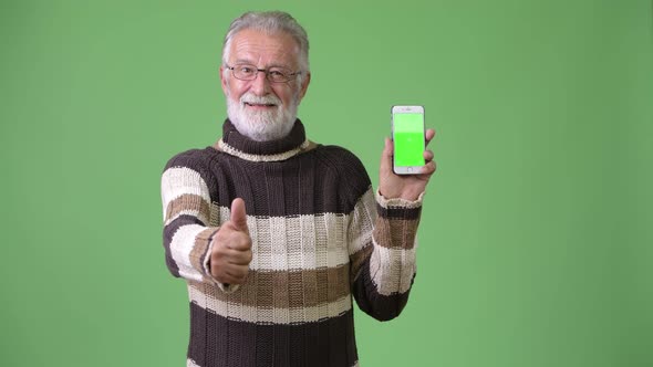 Handsome Senior Bearded Man Wearing Warm Clothing Against Green Background