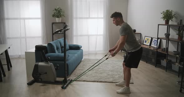 Sportsman Is Training His Body at Home Workout with Sporty Rubber Band in Living Room Tensing