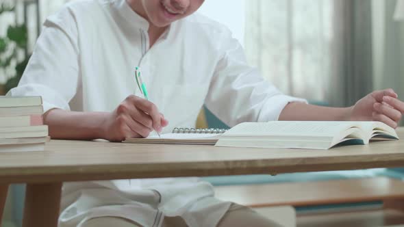 Close Up Of A Happy Asian Man Student Writing In Notebook On The Table While Studying At Home