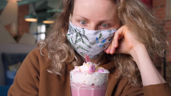 Woman Wearing Protective Face Mask In Cafe Looking At Pink Coffee Latte With Whipped Cream