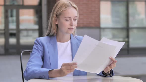 Young Businesswoman Reading Documents while Sitting Outdoor