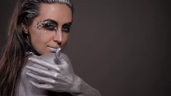 Woman with Silver Paint on Her Skin Face and Hair Poses in a Studio with Chain