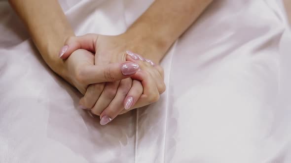 Woman Holds Hands with Pink Glitter Manicure on White Fabric