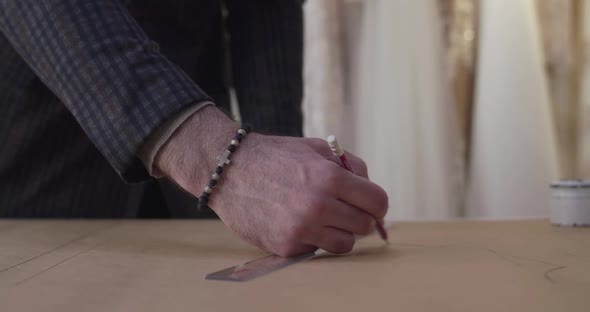 Close View of Tailor's Hand Drawing Curve on Tissue on Desktop in Dress Atelier