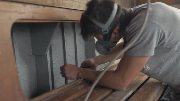 Young man wearing mask painting interior walls of wooden boat