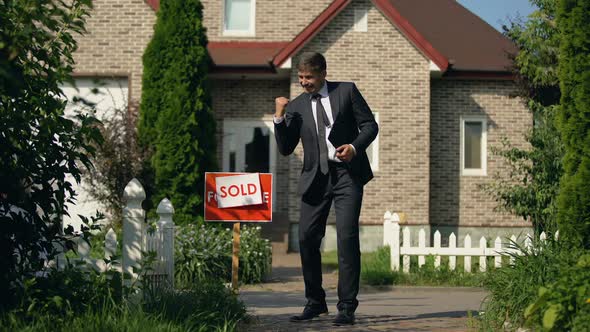 Estate Agent in Business Suit Showing Yes Gesture Standing in Front of Sold Home