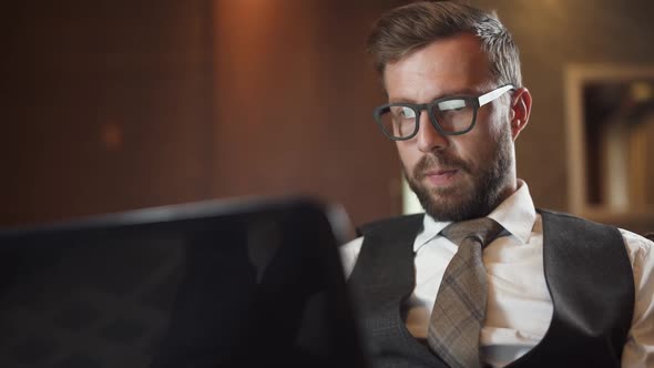 Young Businessman in Glasses Working at a Laptop Man in the Suit Sitting on the Couch in the Hotel