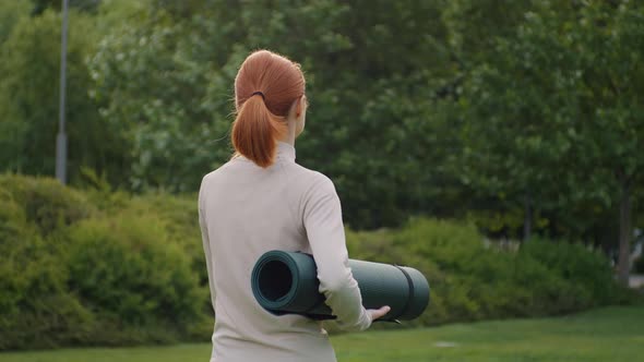 Yoga trainer carry yoga mat in the park, back view.