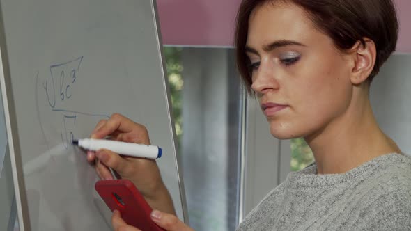 Beautiful Female Student Using Her Smart Phone While Solving Math Problem