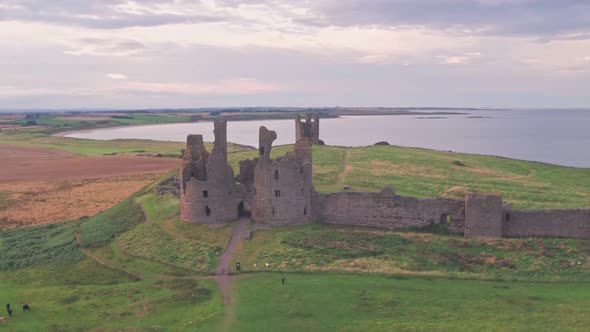 Dunstanburgh Castle at sunset in Northumberland, England, UK, Aerial drone reveal