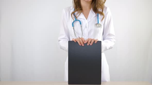 A doctor in a medical gown fills out paperwork on a tablet