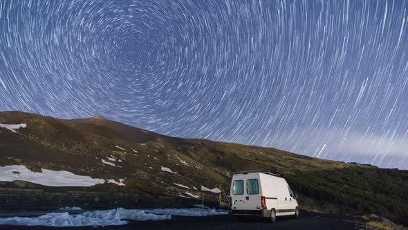 Time lapse of night sky and fog over Etna vulcano mountain with camper van in foreground in winter t