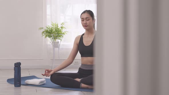 Asian woman does morning yoga, sitting in Easy position, Sukhasana posture, and meditating.