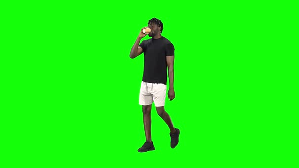 African American Man Is Walking and Drinking Coffee at Green Screen, Chroma Key. Slow Motion