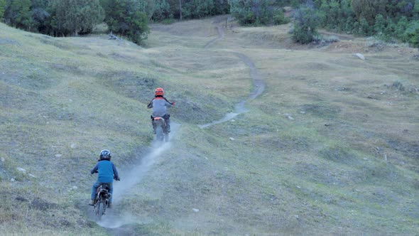 Son follows his dad on a motorcycly along a dusty mountain trail - slow motion