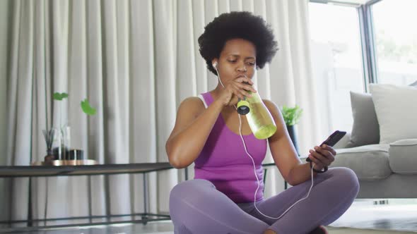 Happy african american wearing sportswear, using smartphone, drinking water