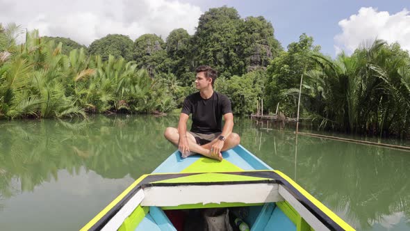 young caucasian man sitting on a boat ride along a river in ramang ramang sulawesi surrounded by man