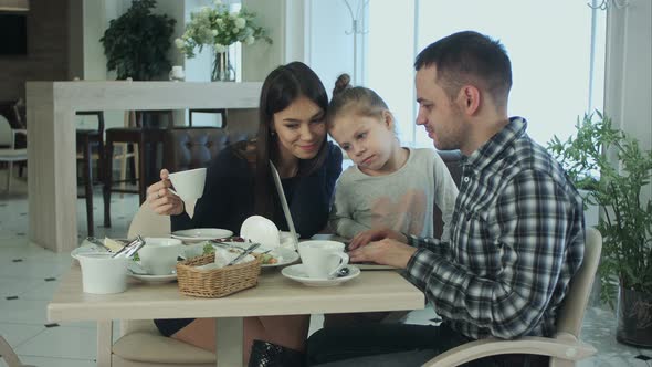 Young Family Using Laptop, Chatting and Smiling in Cafe or Restaurant