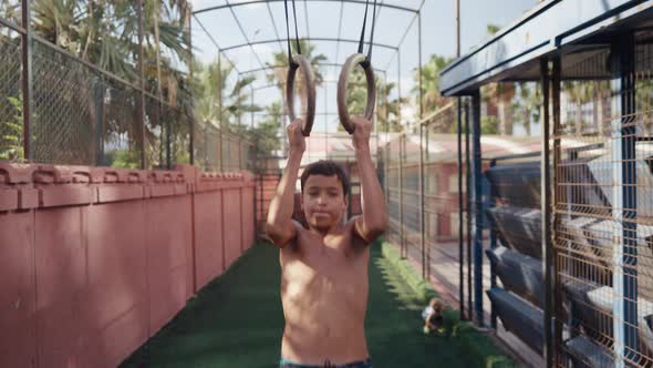 Young Athletic Boy Doing Exercise on the Gymnastic Rings at Street Workout Place