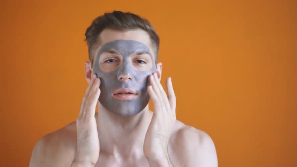 Handsome Man with a Gray Clay Mask on His Face Poses for the Camera on an Isolated Yellow Background