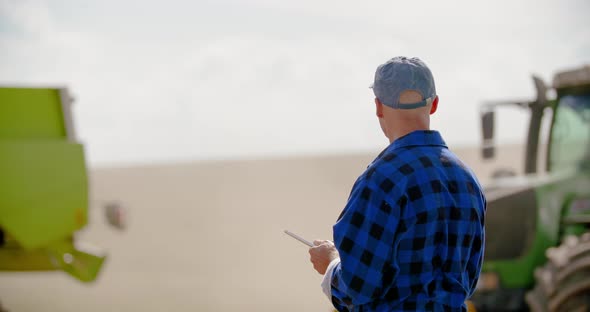 Farmer Using Digital Tablet While Looking at Tractor in Farm
